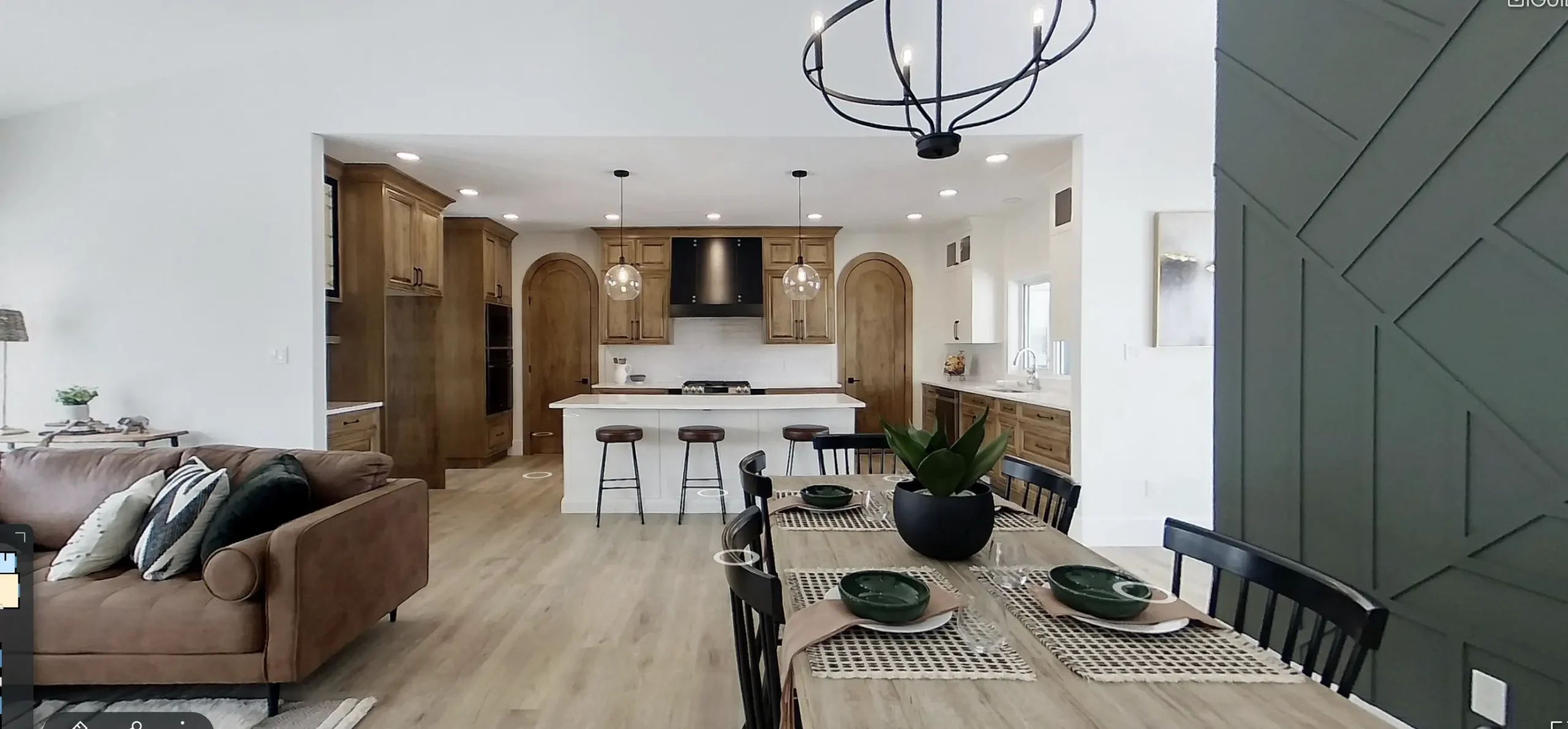 Open concept RTM home in Alberta or Saskatchewan with natural wood kitchen cabinets, arched doors, white island with three stools, black range hood, modern chandelier, and a dining table beside a green accent wall.